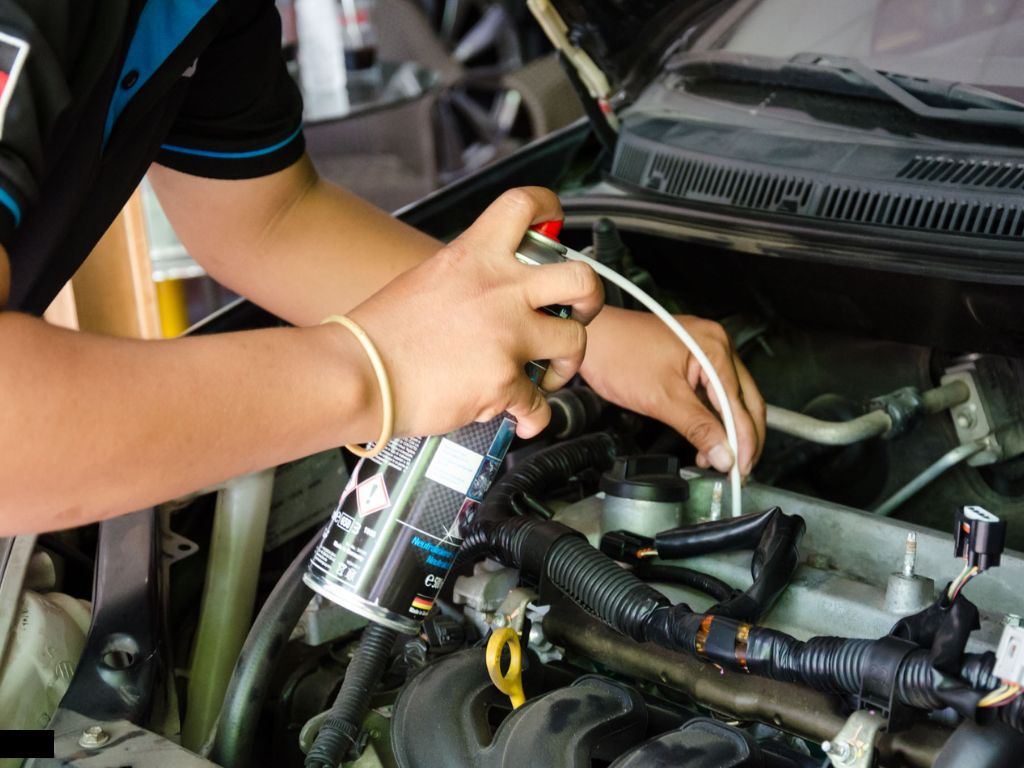 Thợ kỹ thuật đang xịt dung dịch vệ sinh buồng đốt vào hệ thống nạp để loại bỏ cặn carbon trong động cơ ô tô.