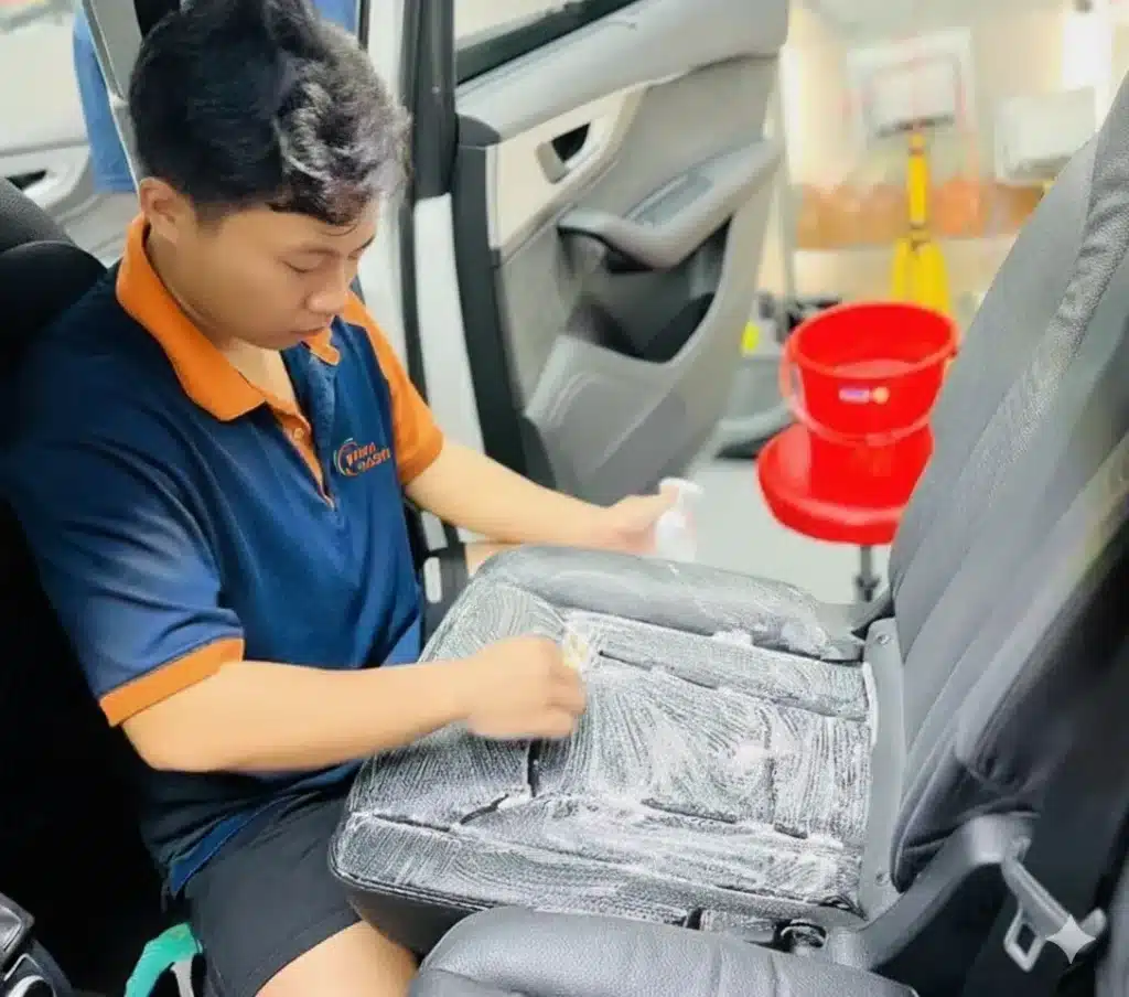 Nhân viên VinaWash đang dùng bàn chải vệ sinh ghế ô tô màu đen,