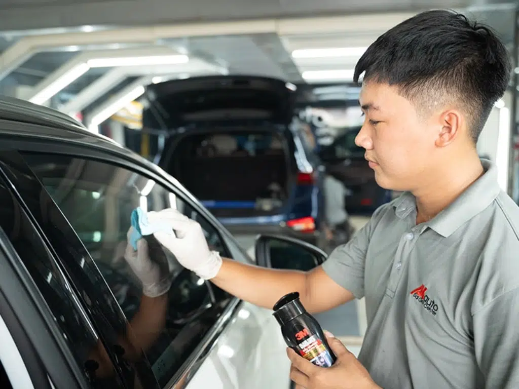 Nhân viên chăm sóc xe đang thi công phủ nano và phủ ceramic cho kính ô tô bằng dung dịch 3M tại gara chuyên nghiệp