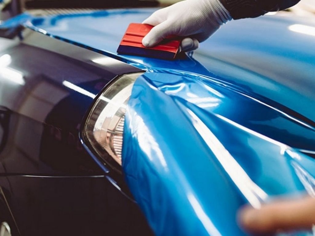 Kỹ thuật viên đang thực hiện thiết kế decal dán xe hơi màu xanh bóng, thao tác tỉ mỉ từng chi tiết.