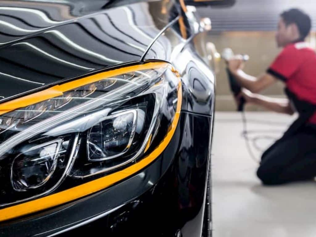 Nhân viên trung tâm chăm sóc xe hơi đang đánh bóng phần đầu xe Mercedes, giúp phục hồi độ sáng bóng của sơn.