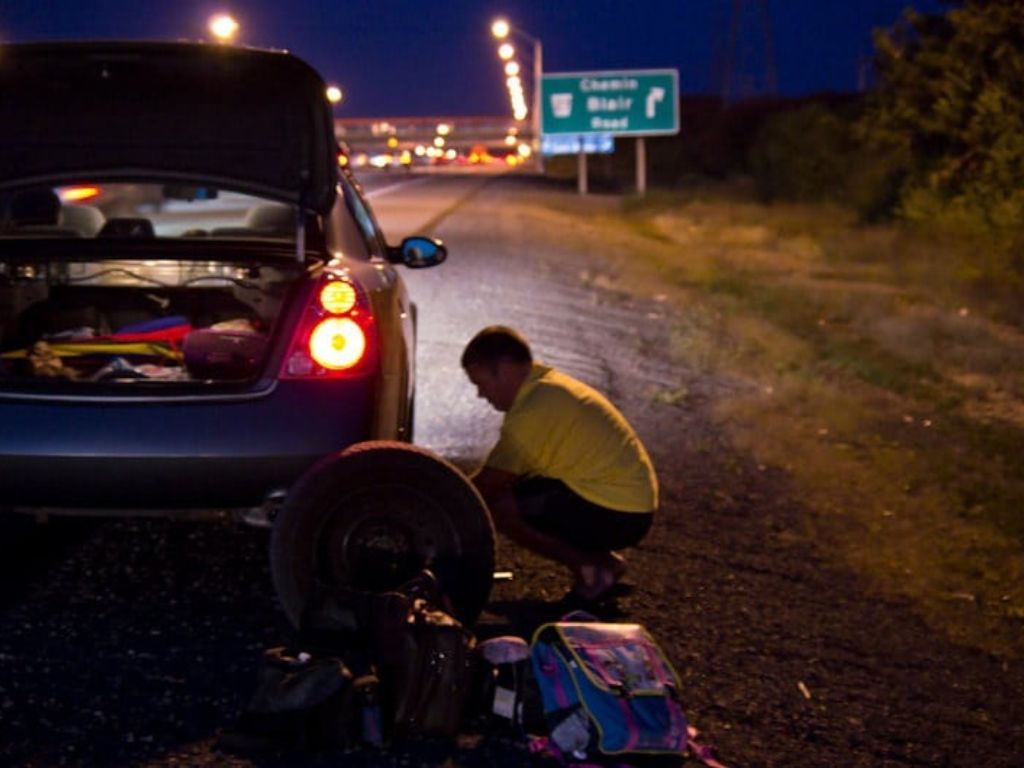 Người lái xe thay và vá lốp ô tô tại nhà bên đường vào ban đêm.