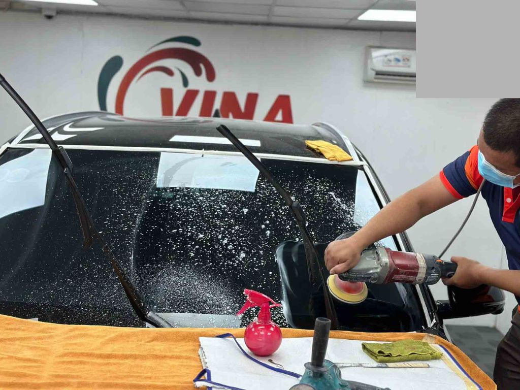 Kỹ thuật viên VinaWash đánh bóng kính ô tô bằng máy chuyên dụng – cách xử lý kính ô tô chuyên nghiệp tại trung tâm.