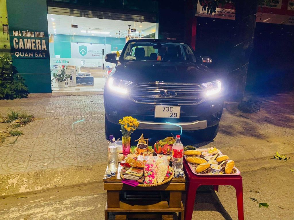 Bàn lễ cúng xe mới buổi tối với mâm cúng đặt trước đầu xe Ford đang bật đèn pha