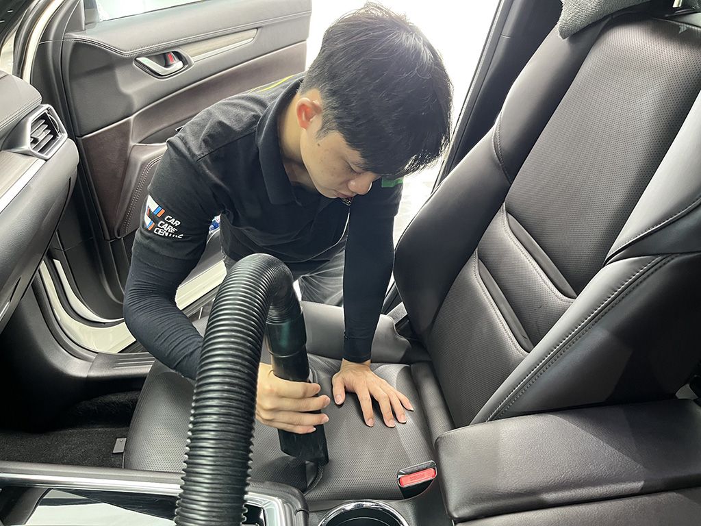Nhân viên dùng máy hút bụi làm sạch bụi bẩn trên ghế da màu đen – dịch vụ vệ sinh ghế da ô tô tại nhà nhanh gọn, hiệu quả cao.