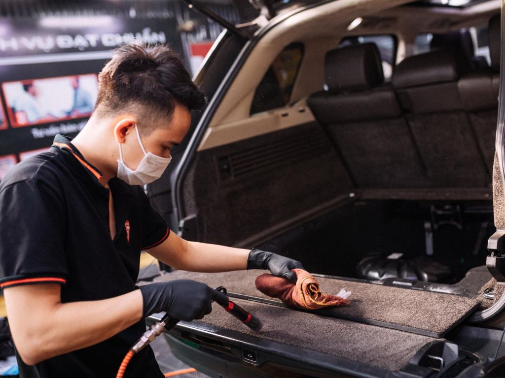 Nhân viên đang vệ sinh cốp sau và bề mặt nội thất xe SUV – dịch vụ vệ sinh ghế da ô tô trọn gói, làm sạch toàn bộ nội thất.
