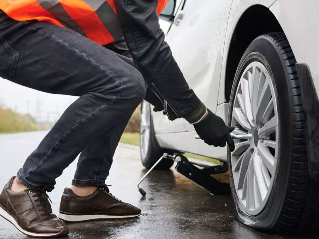 Thay lốp xe ô tô bị nổ lốp giữa đường, người lái xe đang sử dụng kích nâng để tháo bánh an toàn.