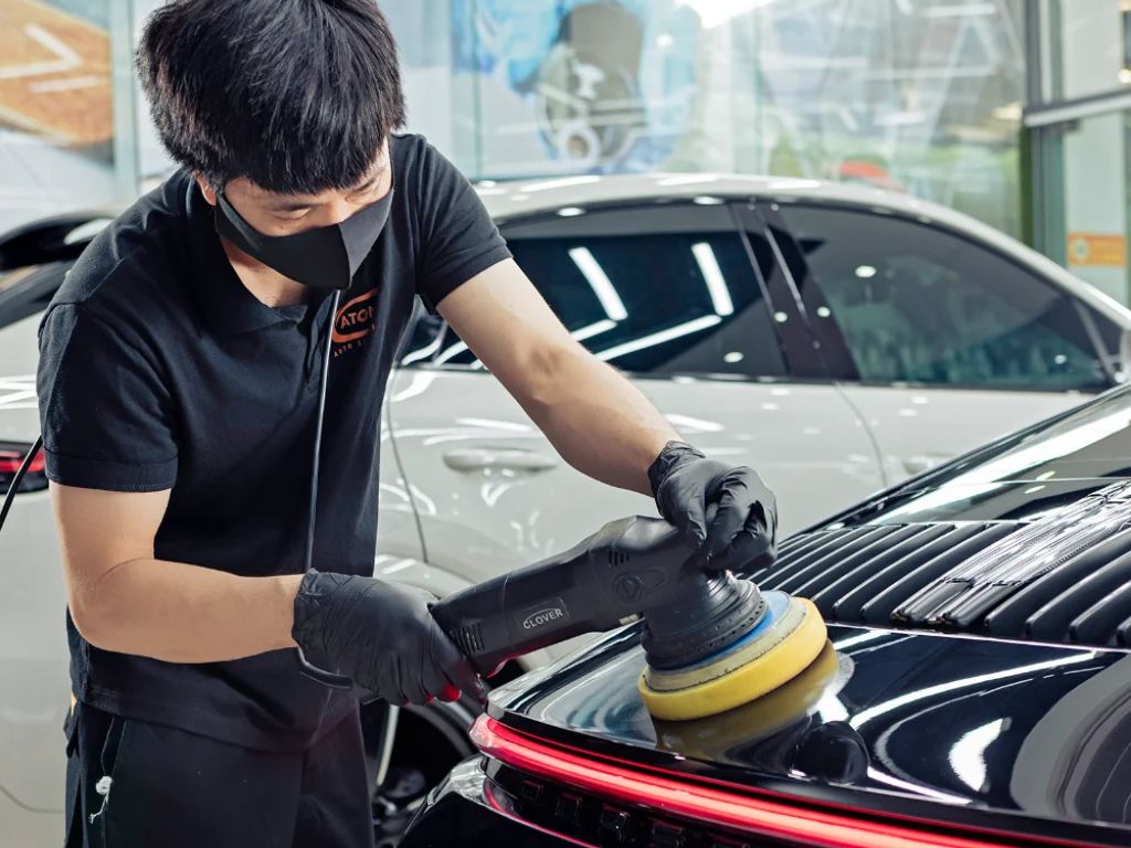 Thợ đang đánh bóng và xử lý xe ô tô bị trầy xước nặng bằng máy đánh bóng chuyên dụng tại gara detailing.