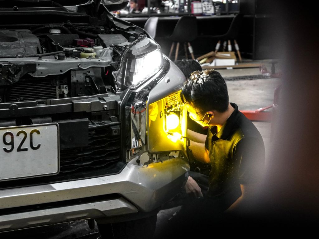 Kỹ thuật viên chỉnh đèn pha ô tô trong xưởng nhằm đảm bảo ánh sáng chiếu đúng tiêu chuẩn.